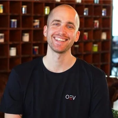 Lächelnder, kahlköpfiger Mann in schwarzem T-Shirt vor einem Bücherregal.